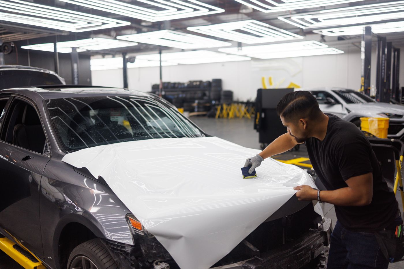 Installer applying white vinyl wrap to a car hood